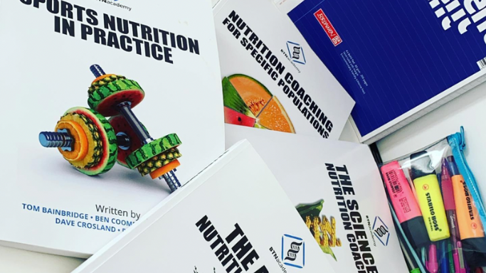 This image shows all four of The BTN Academy's Advanced Nutrition Coaching Course textbooks spread out on a table, with an A4 notebook and a clear pencil case full of pens and highlighters next to them.